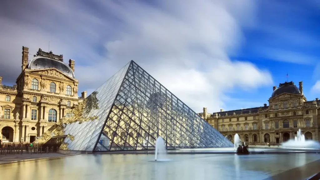 Aerial view of the Louvre Museum with the iconic glass pyramid Tourists queuing to view the Mona Lisa inside the Louvre Museum The glass pyramid of the Louvre Museum during peak tourist hours